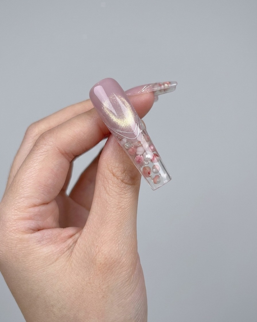 Une pince déposant un petit nœud en cristal 3D brillant sur un ongle.