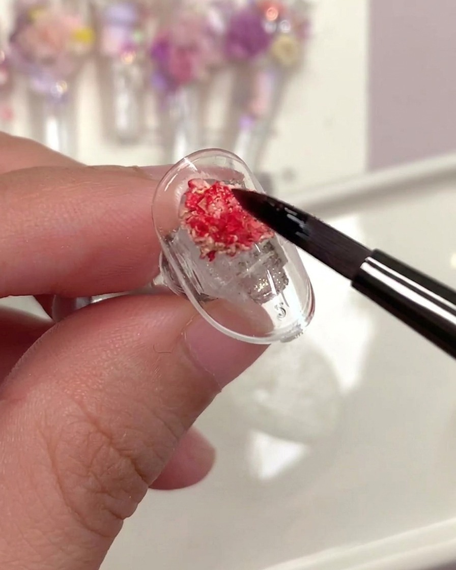 Un pinceau appliquant un top coat transparent sur une rose séchée sur un ongle.
