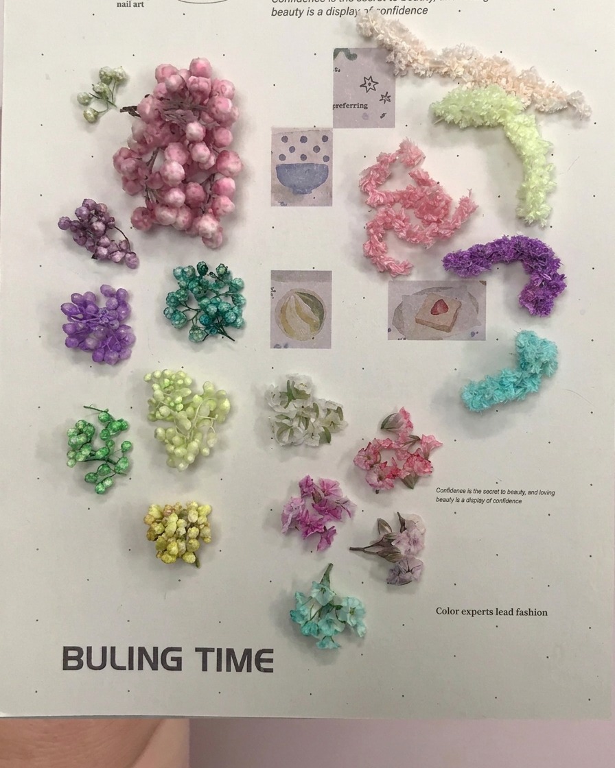 Une pince dorée saisissant de petites boules de fleurs séchées violettes sur une surface plane.