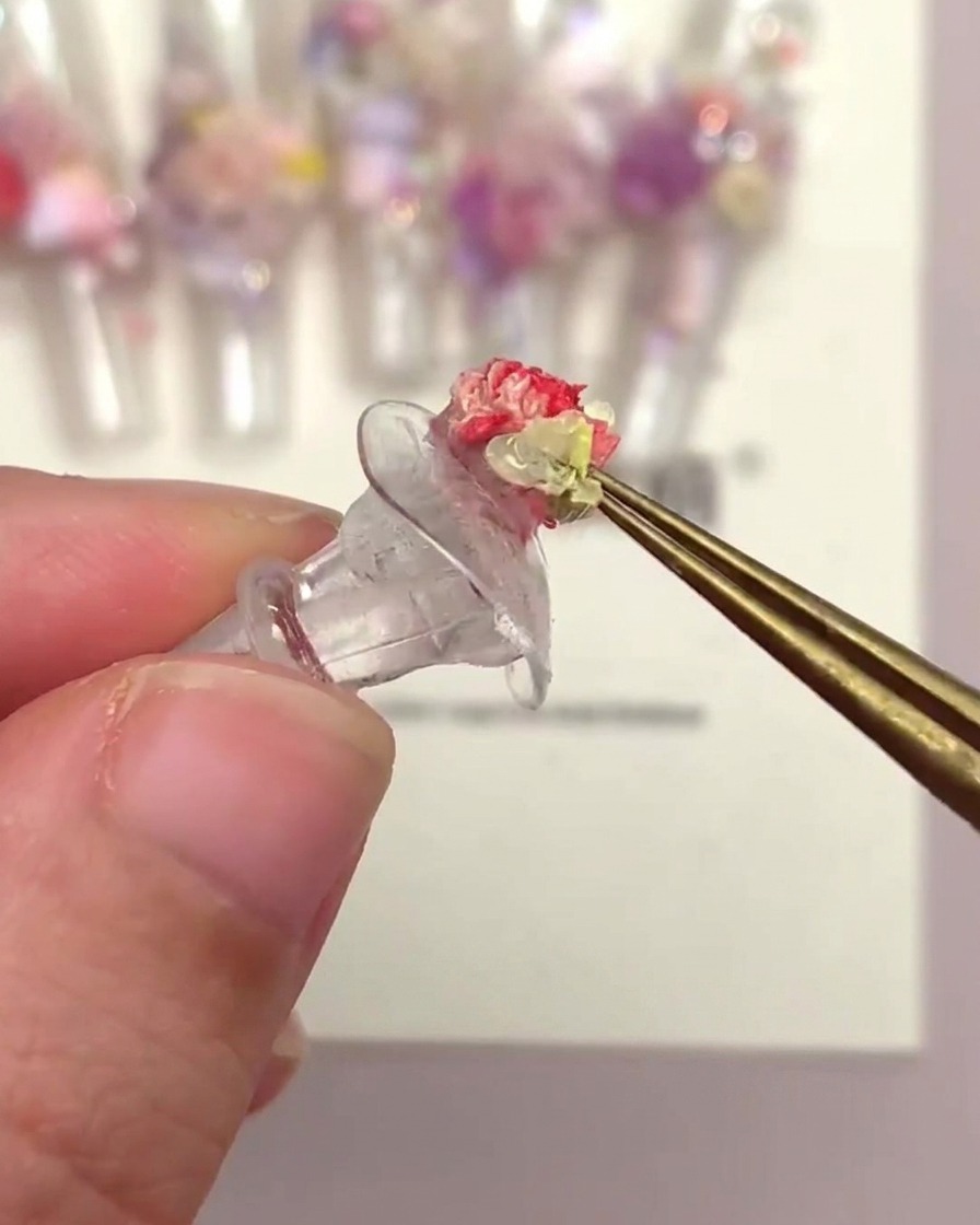 Une main utilisant une pince pour placer une tête de fleur en trompette sur un tip décoré avec dautres fleurs.