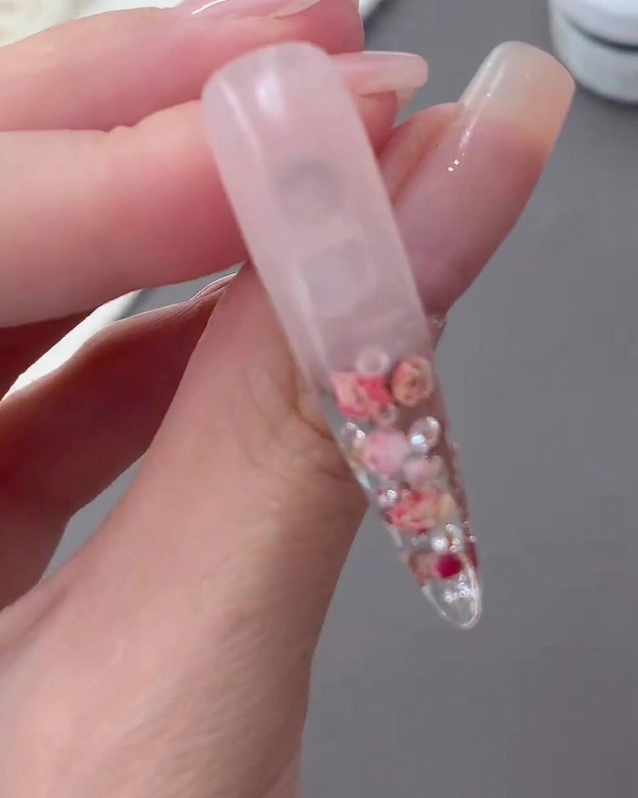 Une capsule transparente catalysée présentée pour montrer le design floral encapsulé et le fond en dégradé laiteux.