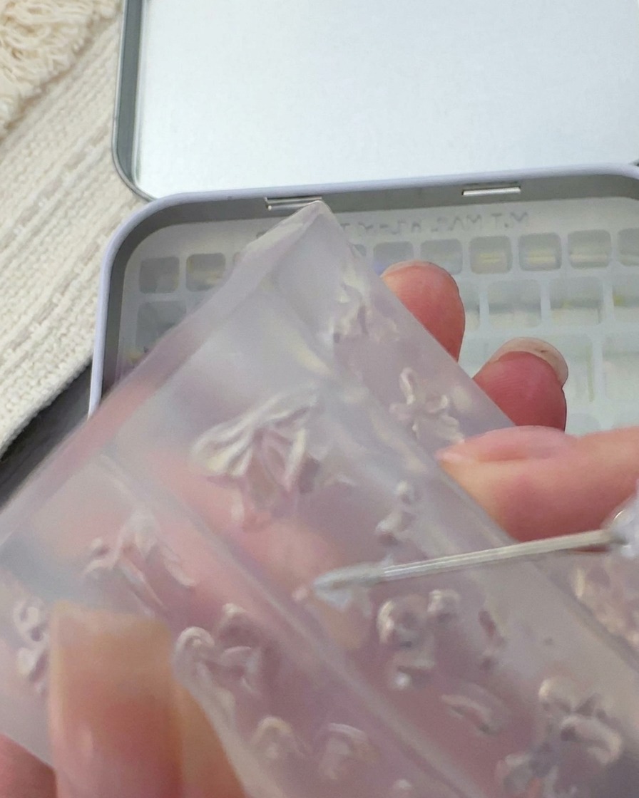 Un outil métallique soulevant un petit nœud 3D blanc délicat dun moule en silicone transparent.