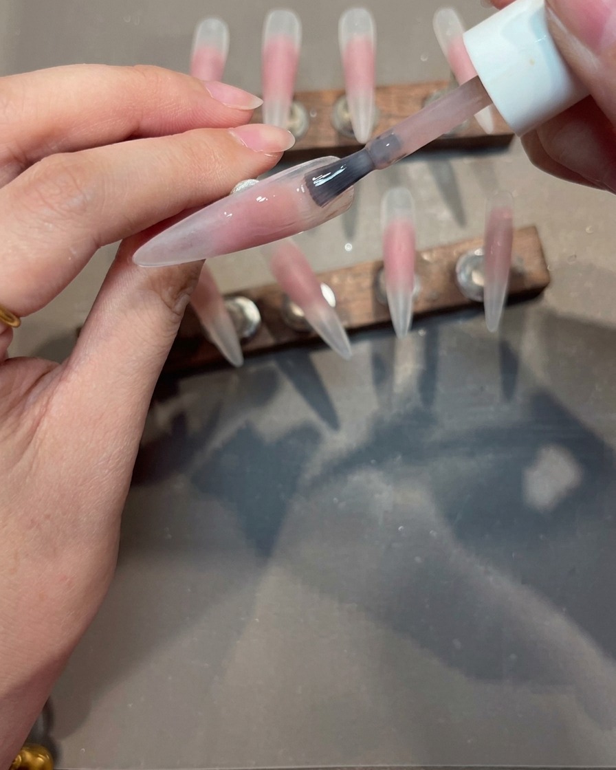 Application dune couche de gel nude sur une capsule au centre déjà coloré en rose.