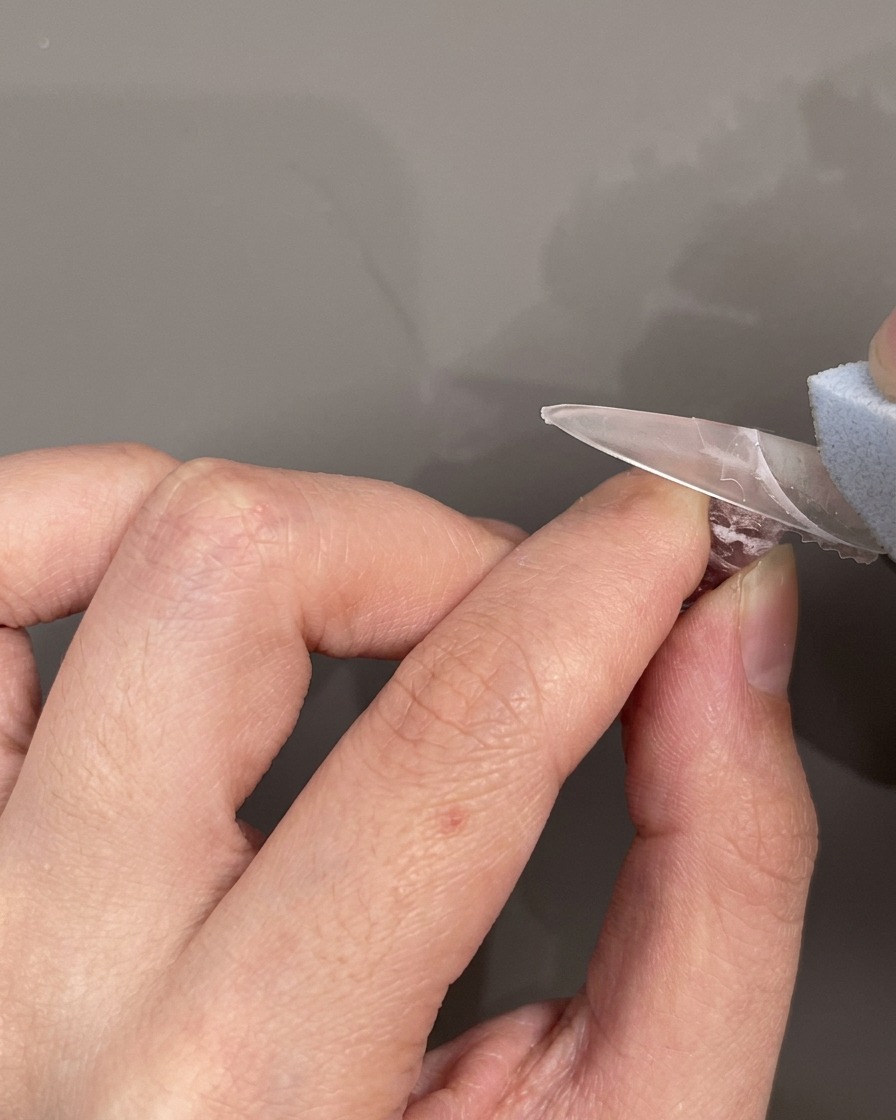 Un guide silicone pour French manucure placé horizontalement sur longle pour délimiter la zone de la pointe.