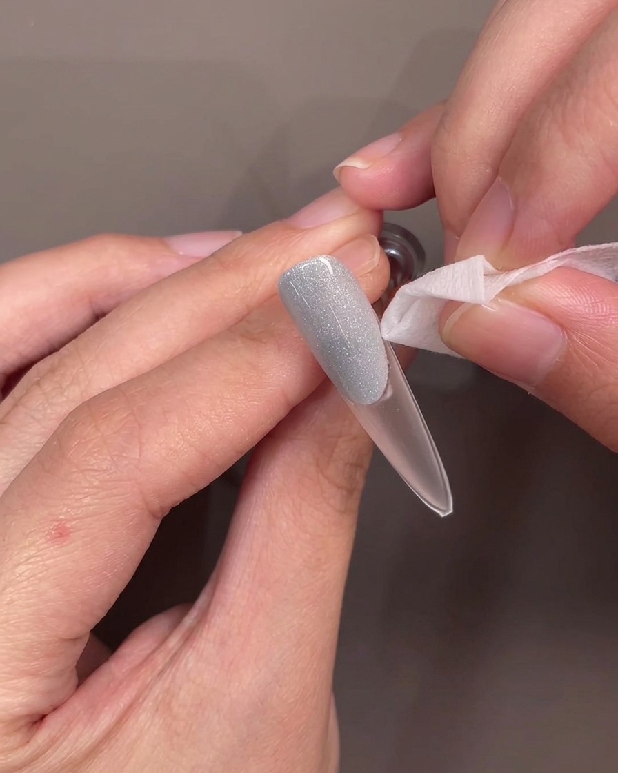 Une pince soulevant délicatement le guide en silicone de longle, révélant un bord net sur le gel bleu.