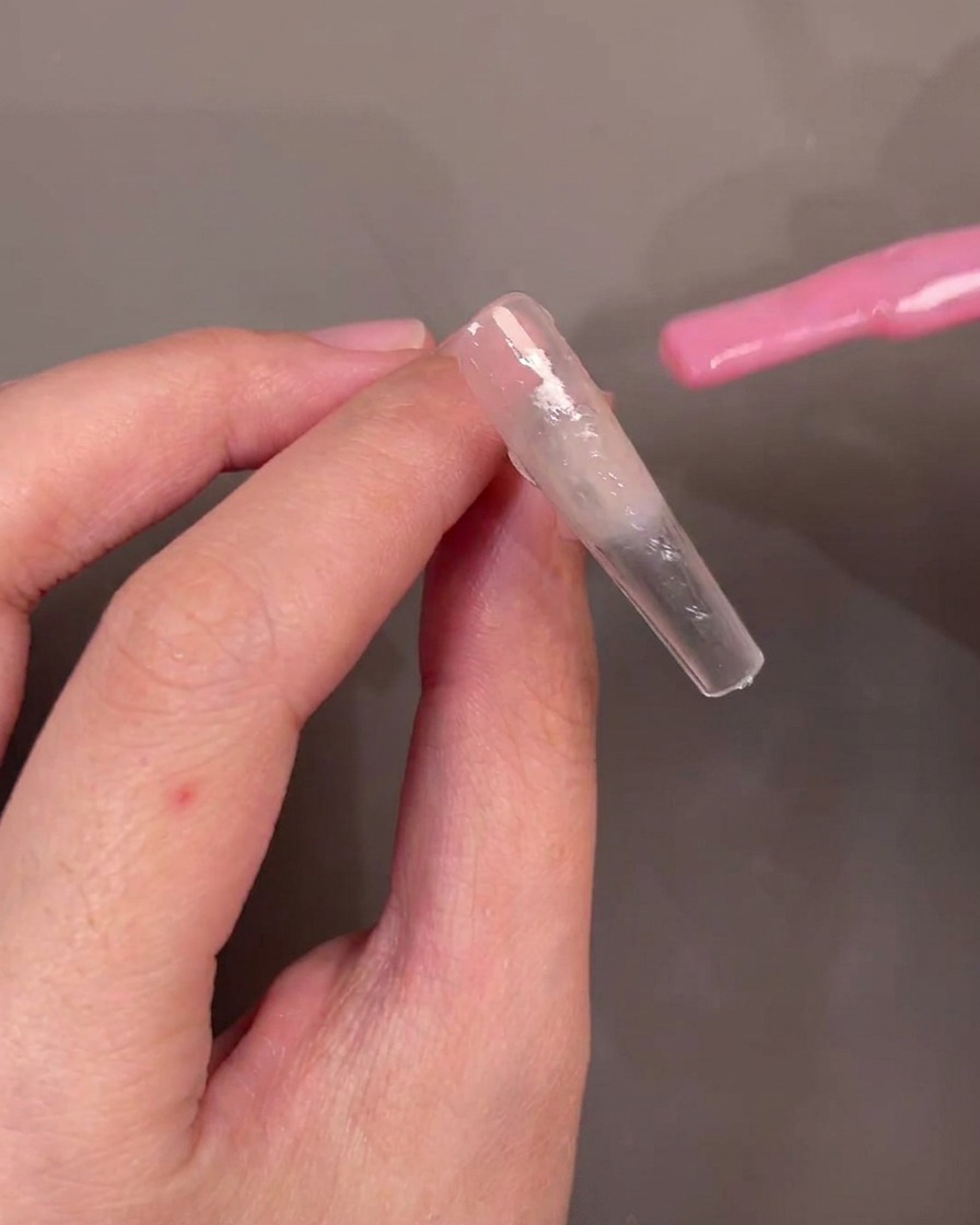 Un pinceau appliquant du gel rose translucide en diagonale sur longle.