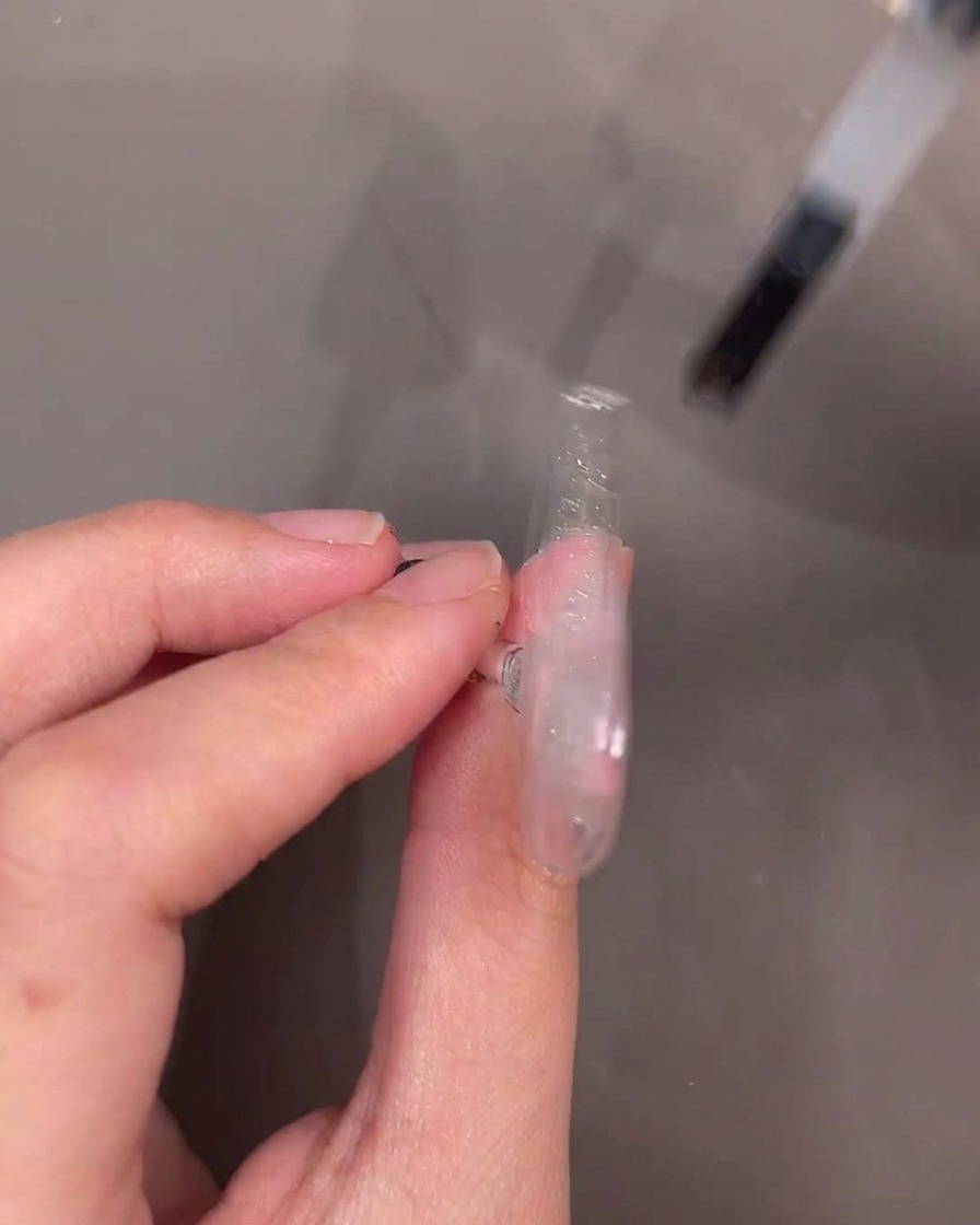 Le pinceau du flacon appliquant une couche de gel de renfort transparent sur longle décoré.