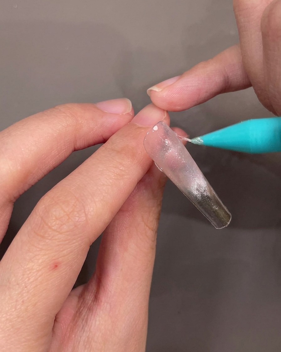 Gros plan sur lapplication dune ligne fine et diagonale de gel pailleté argenté sur longle.