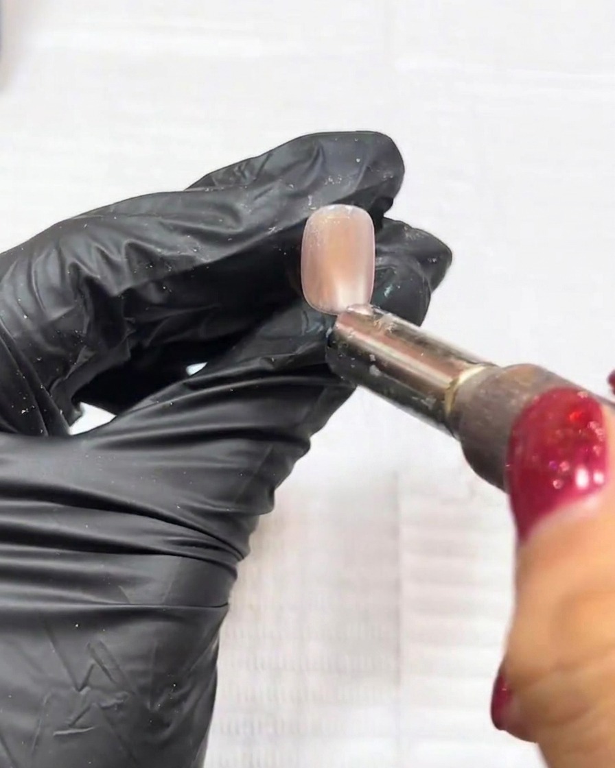 Gros plan sur lutilisation dun aimant au-dessus dun ongle pour manipuler les particules cat-eye en un point central défini.