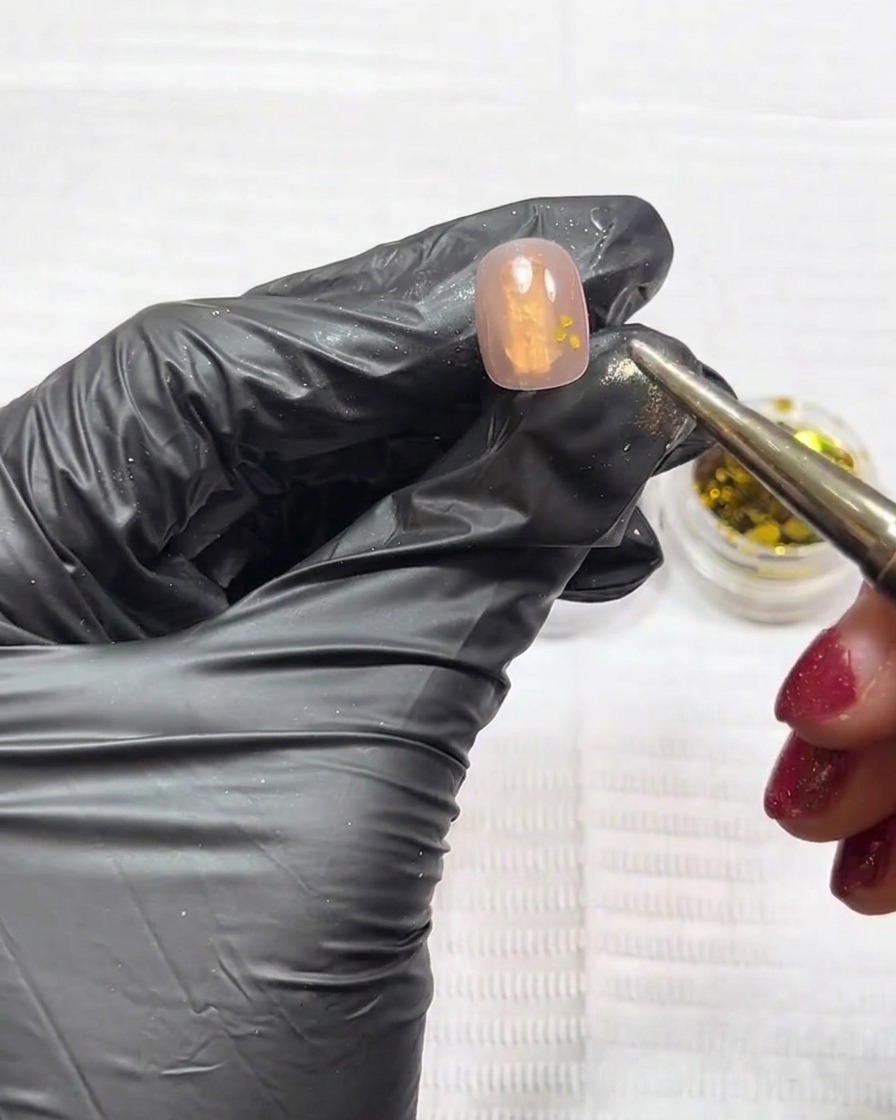 Gros plan dun ongle avec des paillettes or et argent placées sur une base nude.