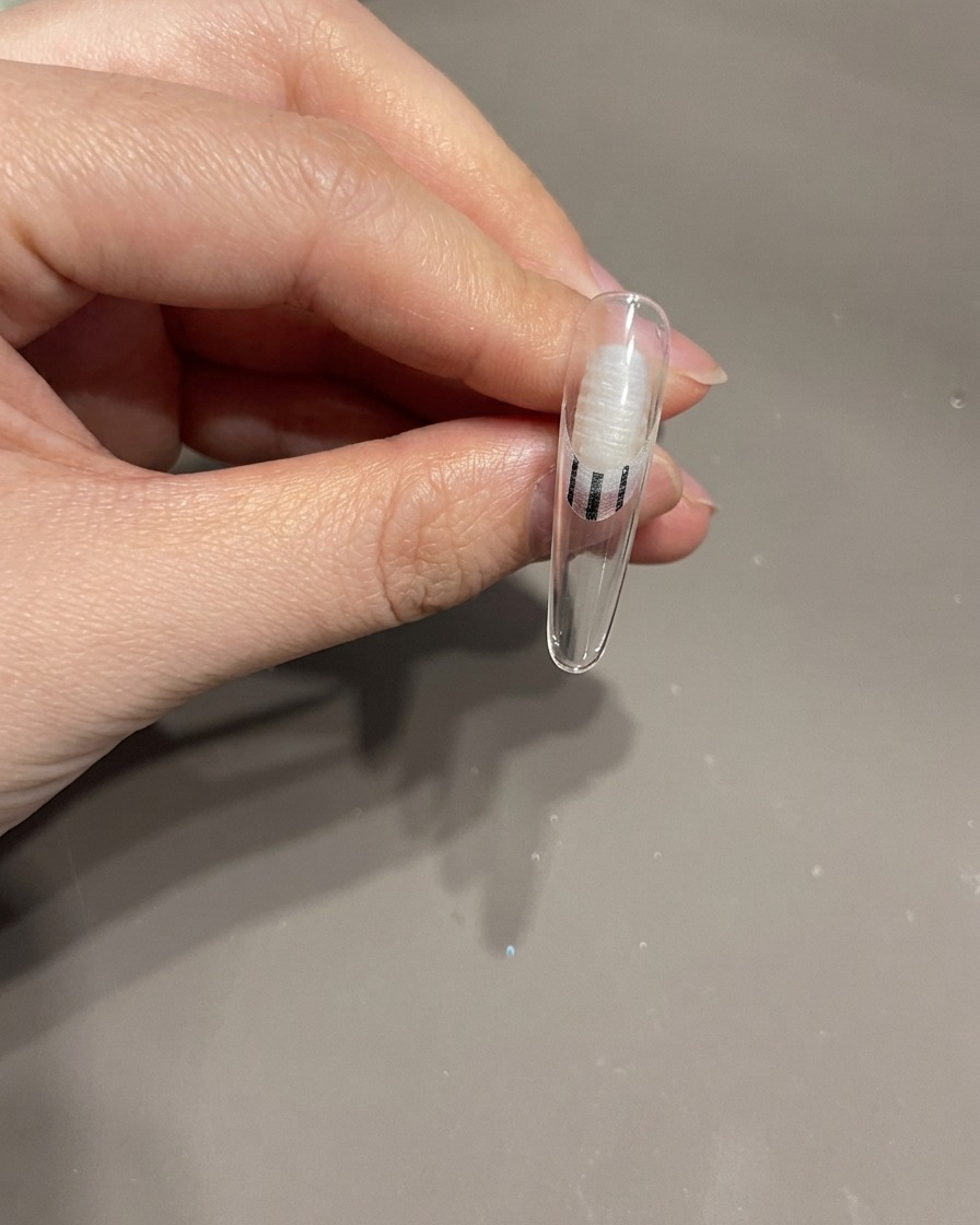 Gros plan dune main plaçant un ongle avec un nœud 3D sous une lampe à ongles UV pour la catalyse.