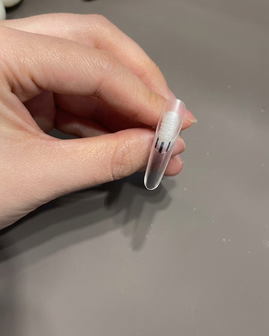 Un pinceau de détail dessinant de fines lignes blanches dans un motif tourbillonnant sur un ongle recouvert de gel.