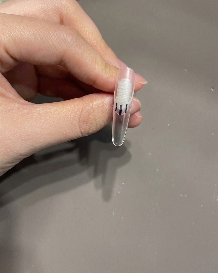 Un pinceau à ongles appliquant une petite goutte de top coat transparent sur la surface dun ongle comme colle pour une décoration.