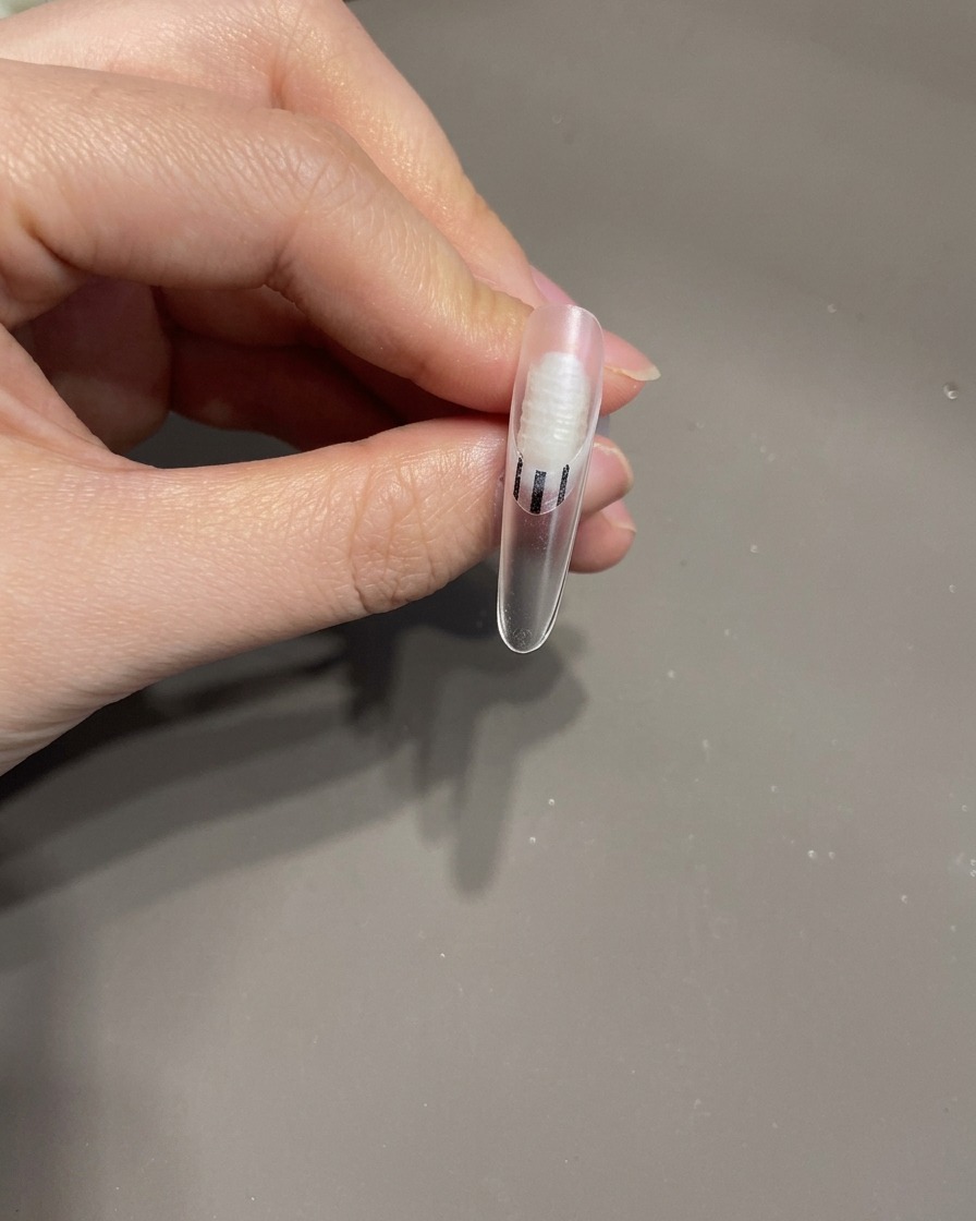 Une pince à épiler plaçant un petit nœud en gel 3D sur la surface dun ongle manucuré.