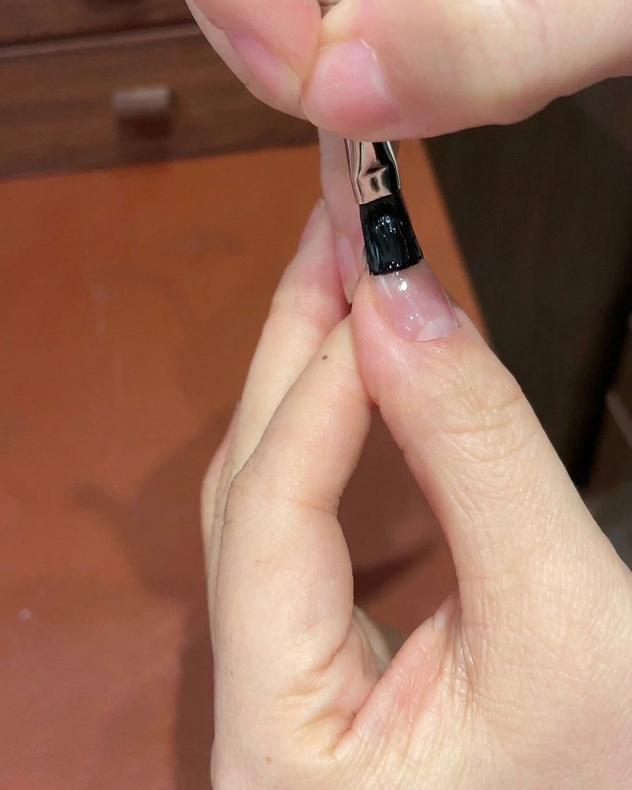 Gros plan dun pinceau de détail appliquant du gel noir sur le bord libre dun ongle.
