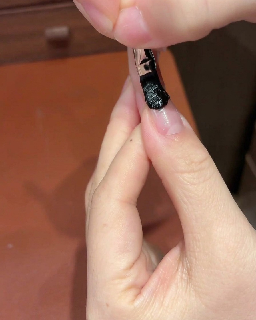 Une éponge cosmétique blanche tapotant une section de gel noir sur un ongle pour créer un dégradé.