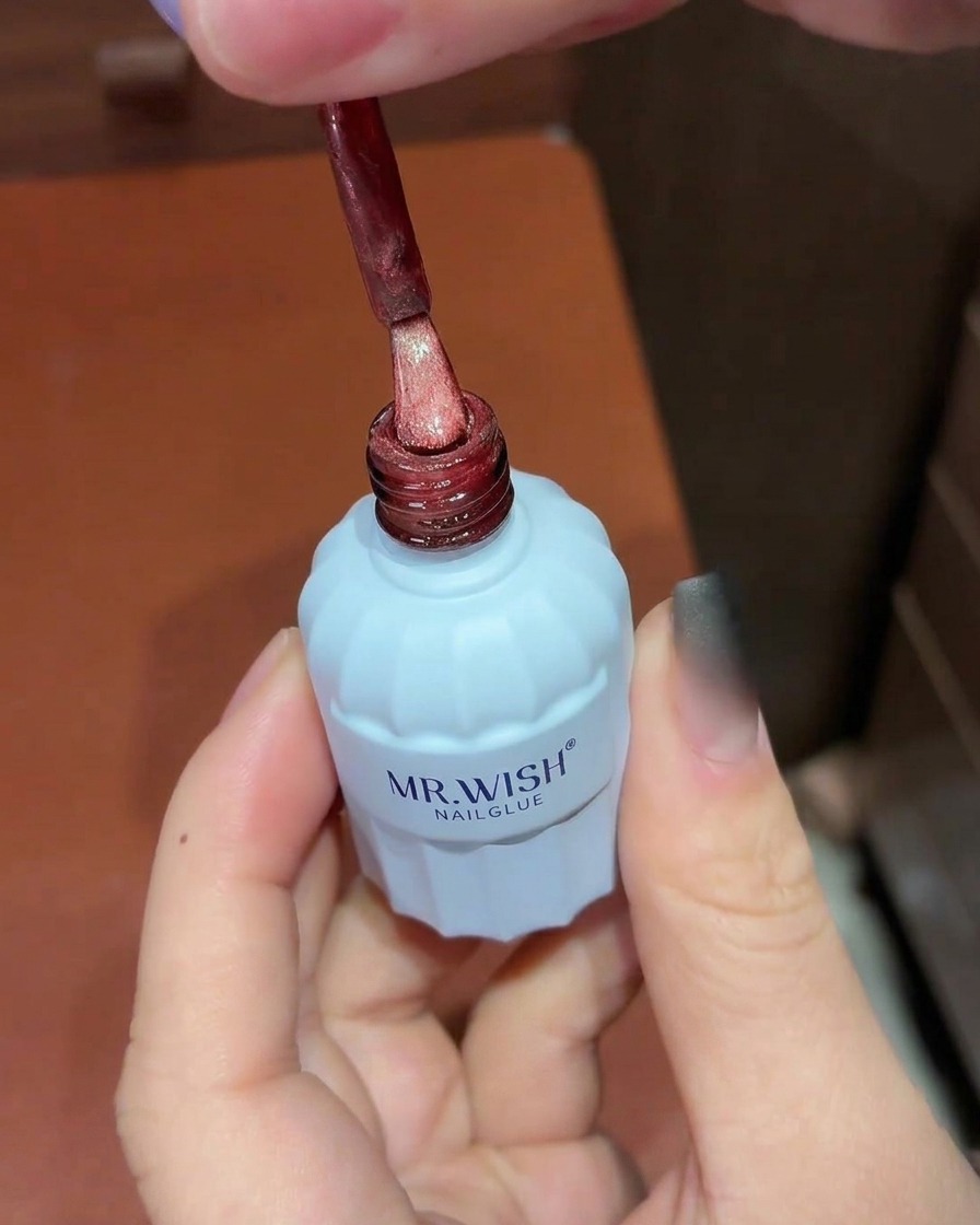 Un pinceau appliquant un vernis gel rouge scintillant effet œil de chat sur un ongle ombré noir.