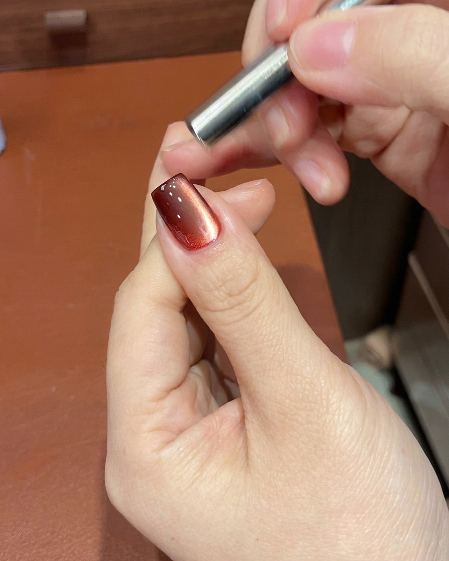 Un outil magnétique positionné près dun ongle pour manipuler les particules scintillantes du vernis gel rouge.