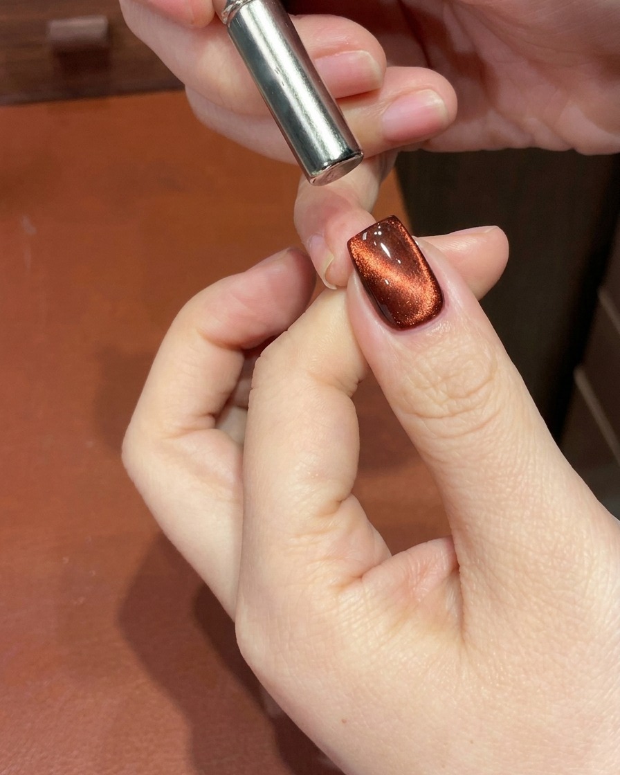 Gros plan dun ongle en gel œil de chat rouge avec un aimant utilisé près de la cuticule pour transformer le reflet en un dégradé profond.