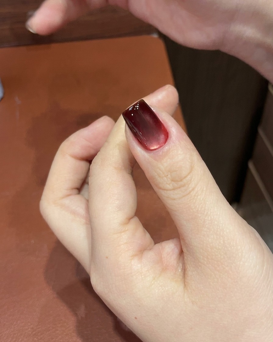 Un ongle en gel œil de chat rouge en train de catalyser sous une lampe UV/LED, révélant une finition brillante et figée.