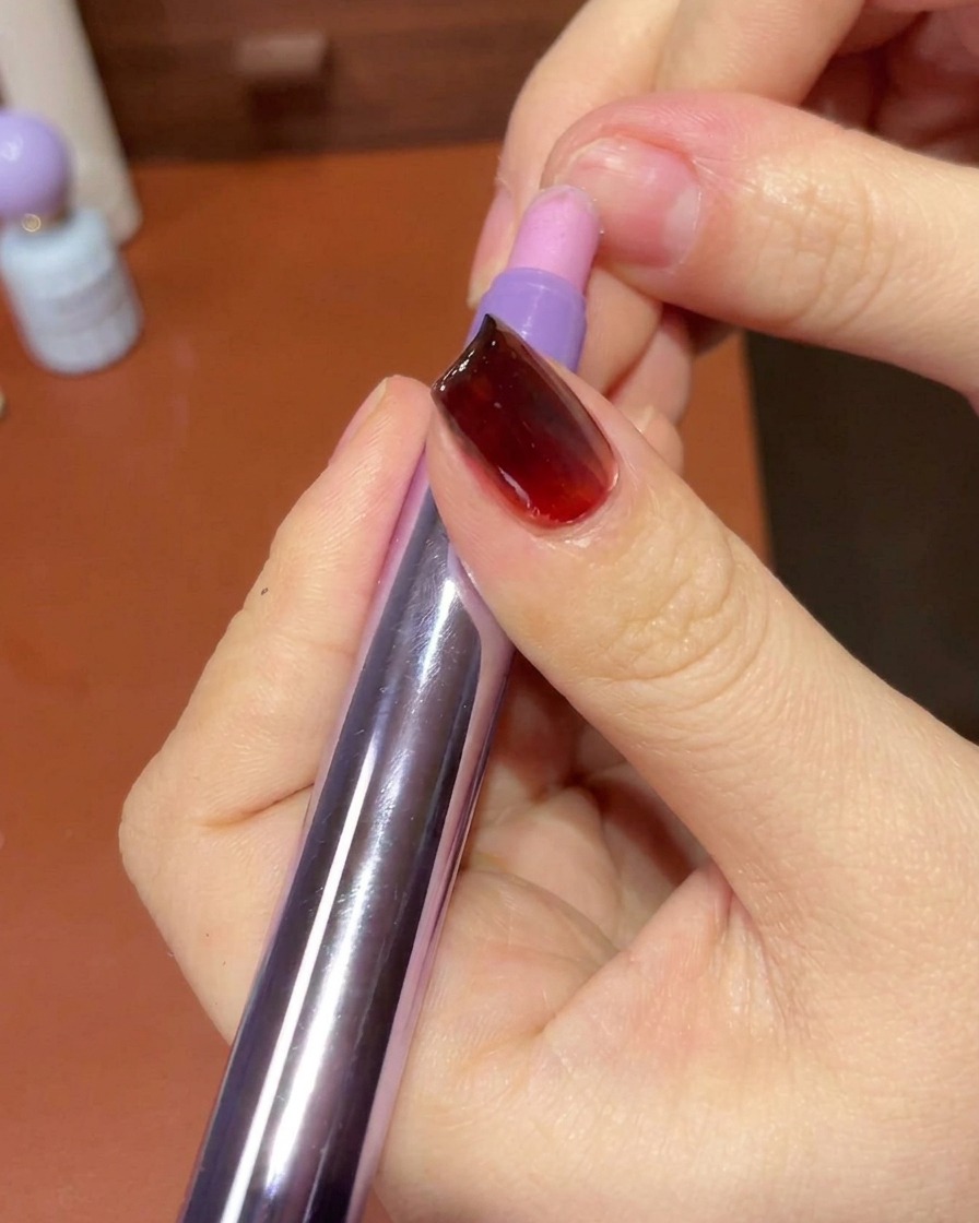 Une main utilisant une lingette non pelucheuse pour nettoyer la peau et les bords autour dun ongle manucuré au gel.