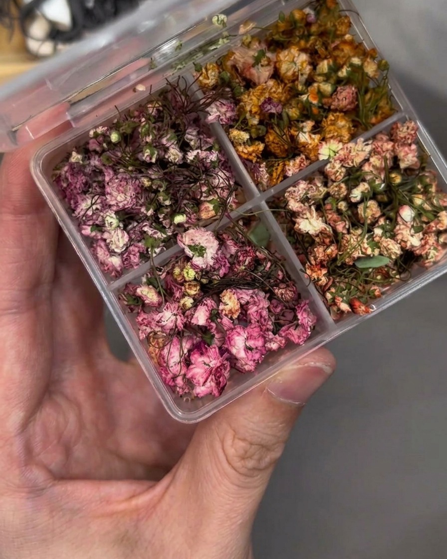 Une pince déposant soigneusement une petite fleur séchée sur un ongle.