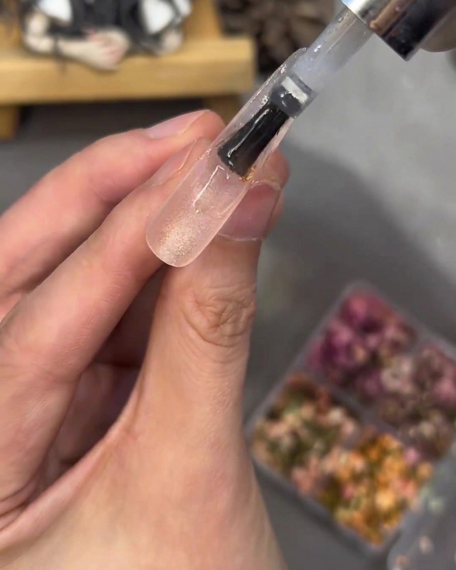Un pinceau appliquant une épaisse couche de gel transparent sur un ongle décoré, lissant ainsi la surface.