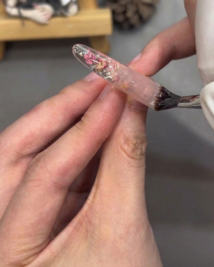 Un pinceau appliquant un top coat transparent sur un ongle décoré pour un fini brillant.