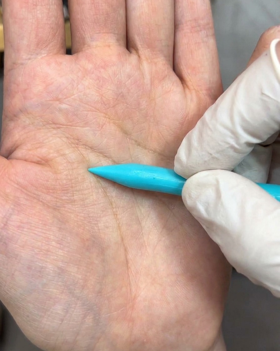Un outil de sculpture pressant une bille de gel blanc sur une surface pour former un pétale.