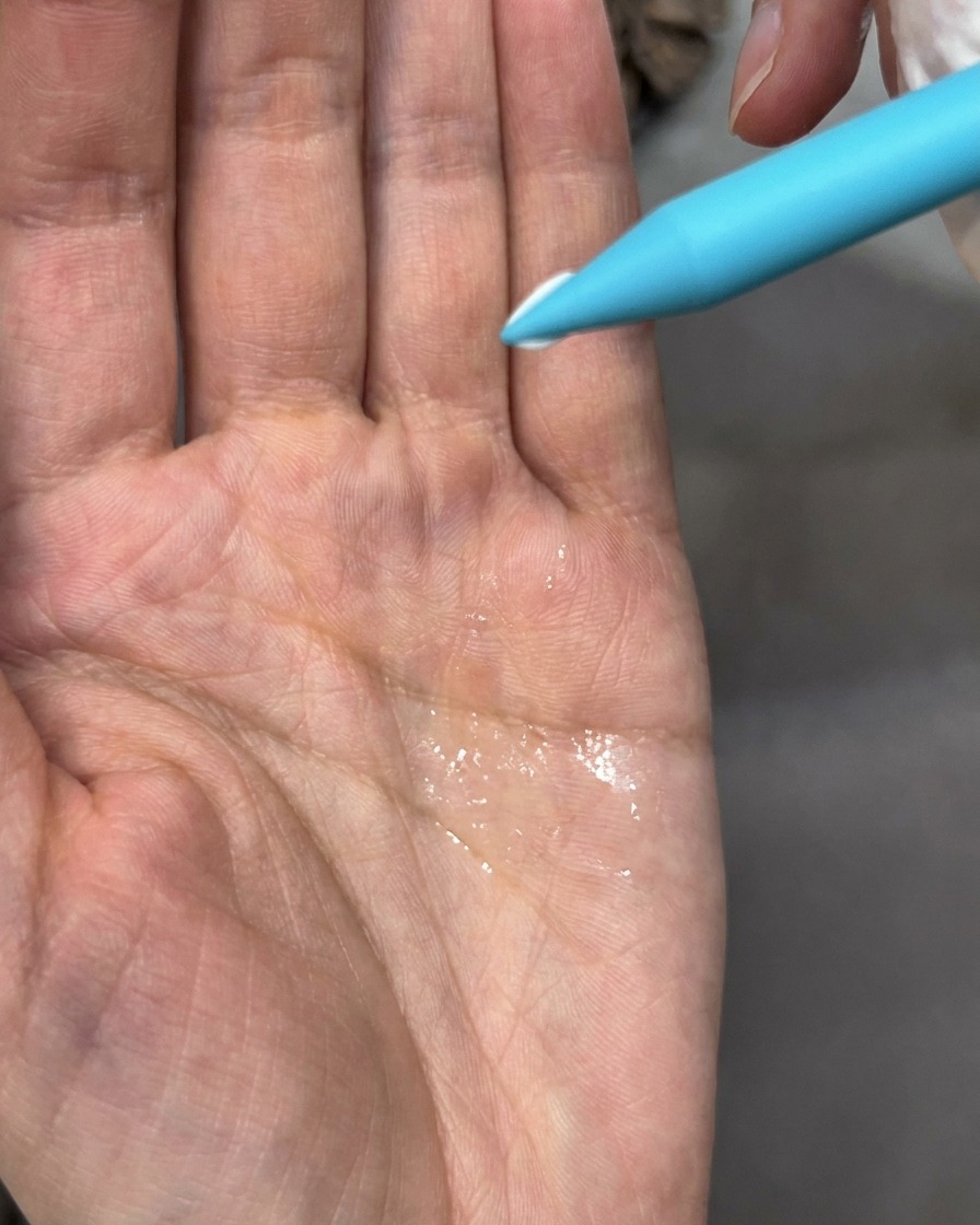 Un pinceau ajustant un pétale blanc sculpté sur un ongle décoré de fleurs séchées.