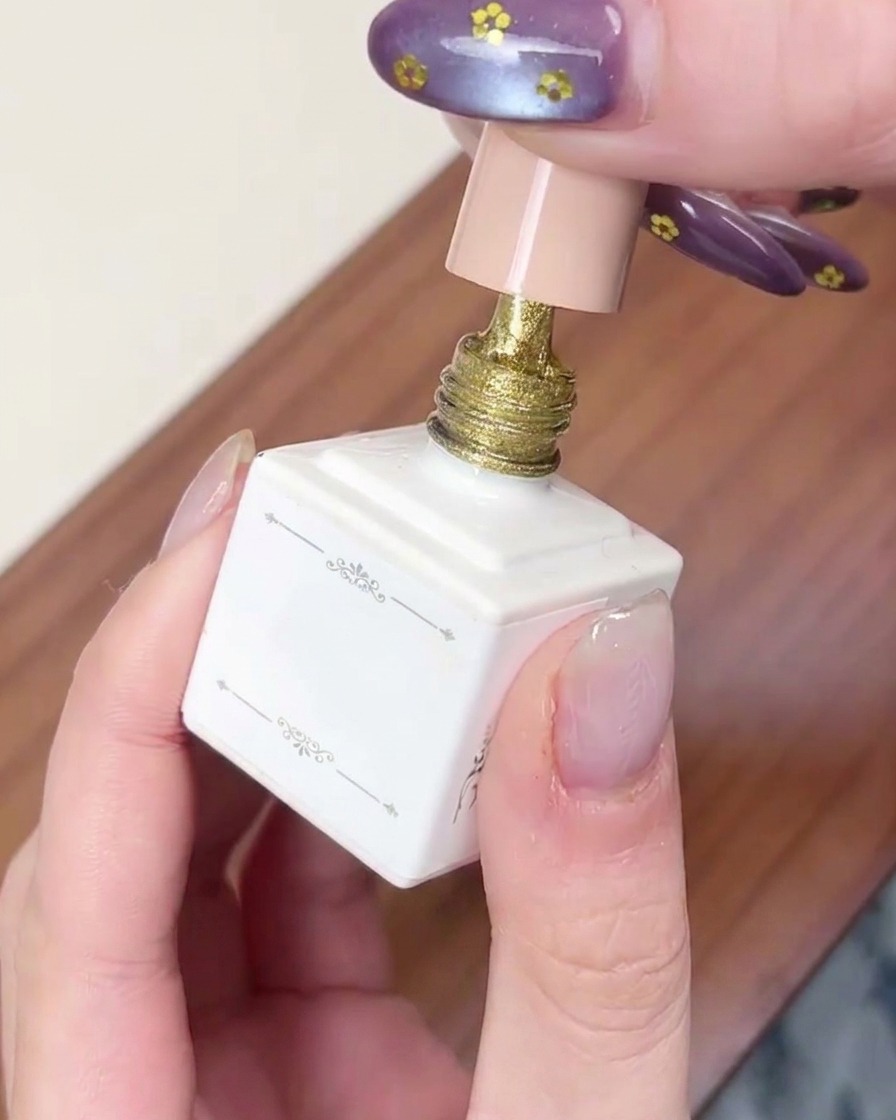 Un pinceau appliquant une couche de vernis gel œil-de-chat doré scintillant sur un ongle.