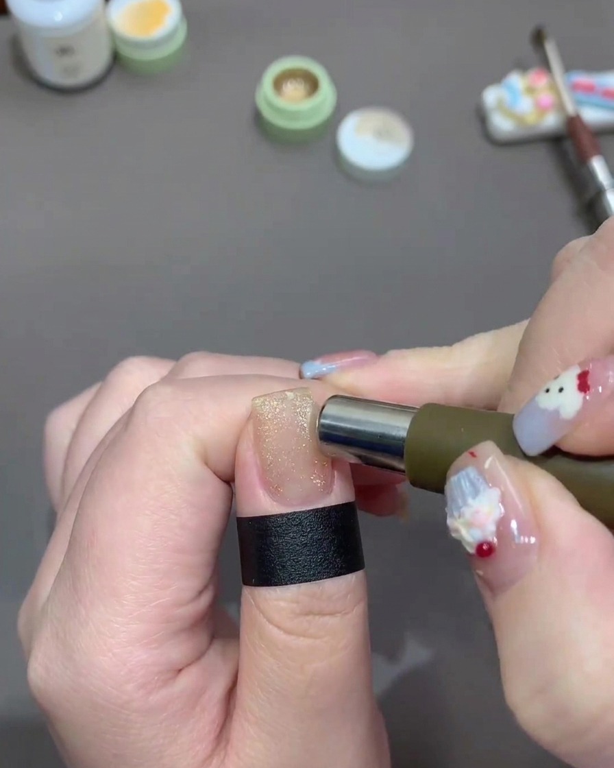 Un aimant cylindrique déplacé sur les bords dun ongle peint avec un vernis gel cat-eye doré étincelant.