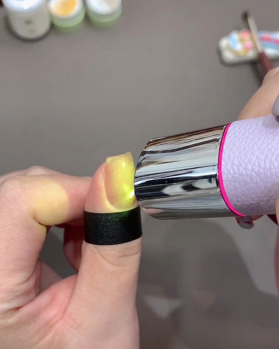 Un ongle brillant intensément sous une petite lampe UV/LED portable pour catalyser le gel.