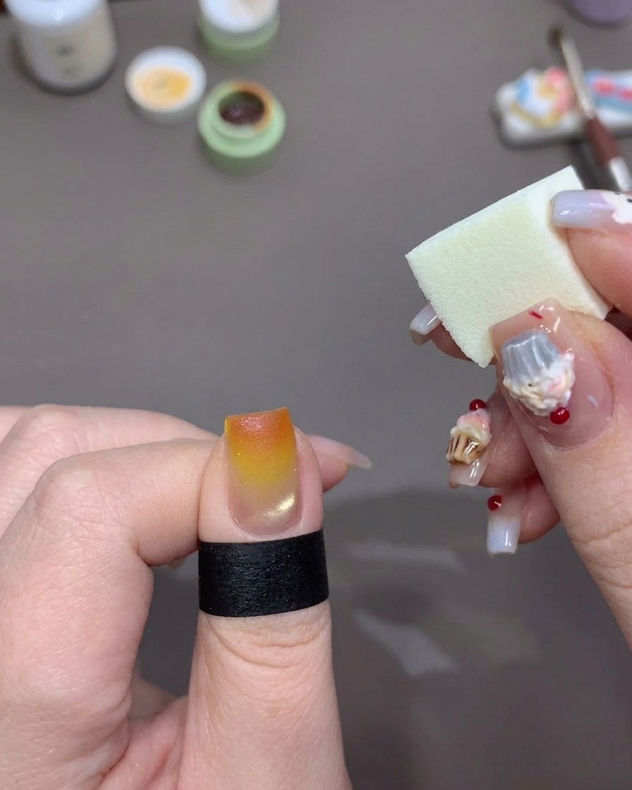 Une éponge de maquillage blanche appliquant du gel orange vif sur le bout de longle pour intensifier leffet coucher de soleil.