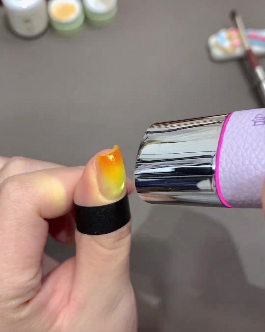 Une mini lampe UV portable placée au-dessus dun ongle pour catalyser un dégradé orange et jaune.