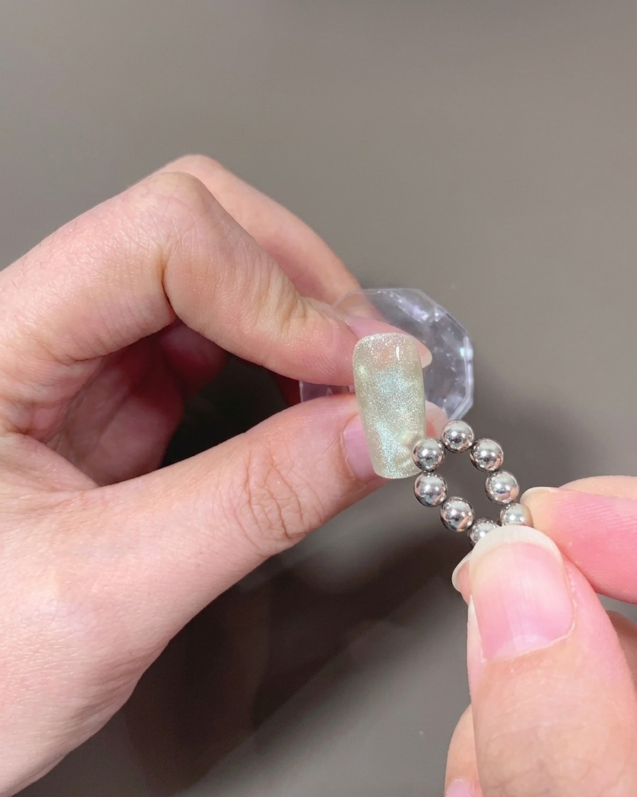 Gros plan dun ongle avec du gel cat-eye non catalysé, un aimant à bout rond créant un motif de vague.
