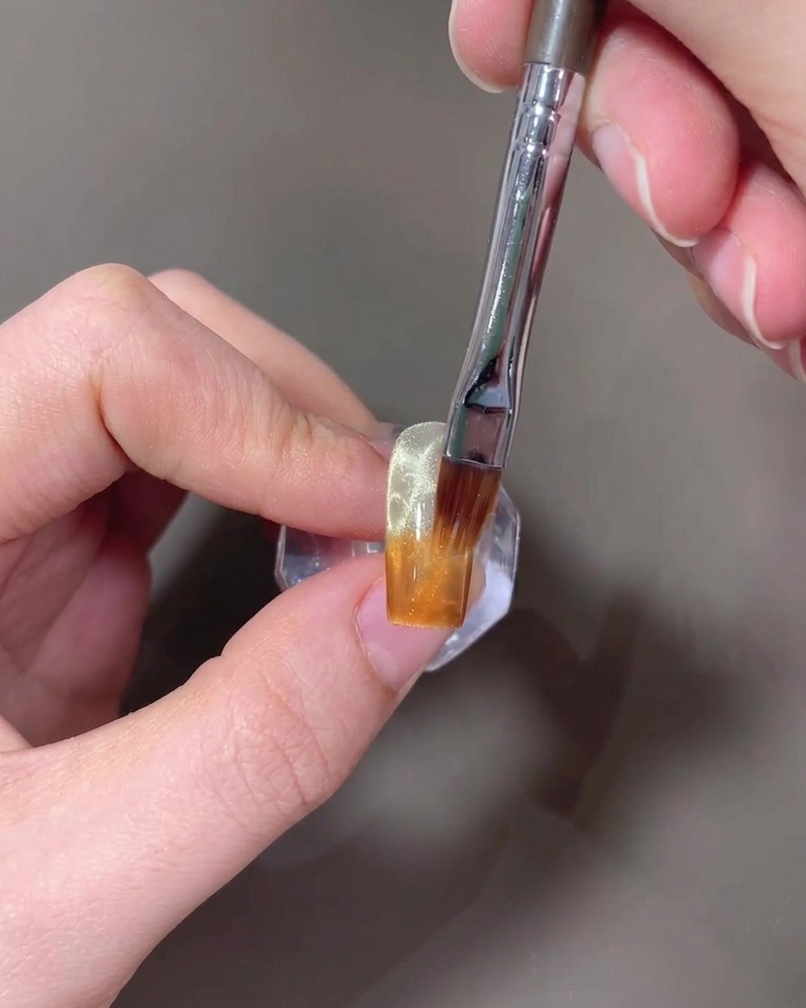 Un pinceau estompant le gel ambre vers le haut sur un ongle pour créer un dégradé.