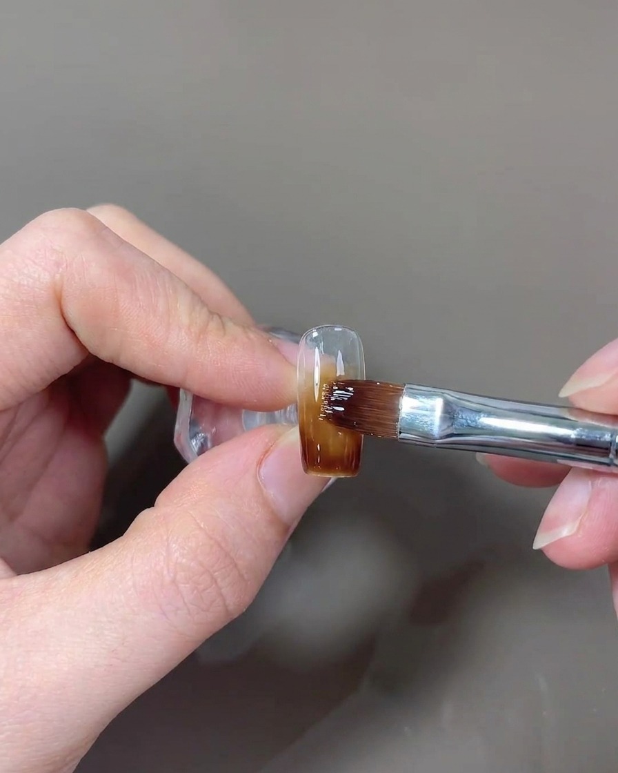 Un pinceau appliquant une dernière couche de top coat brillant sur longle.