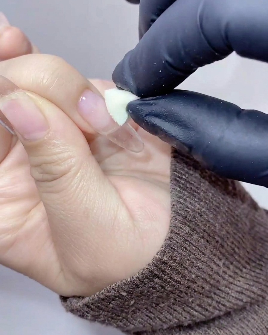 Mains gantées utilisant une petite éponge cosmétique pour tamponner du gel pêche-orangé sur le centre de longle.
