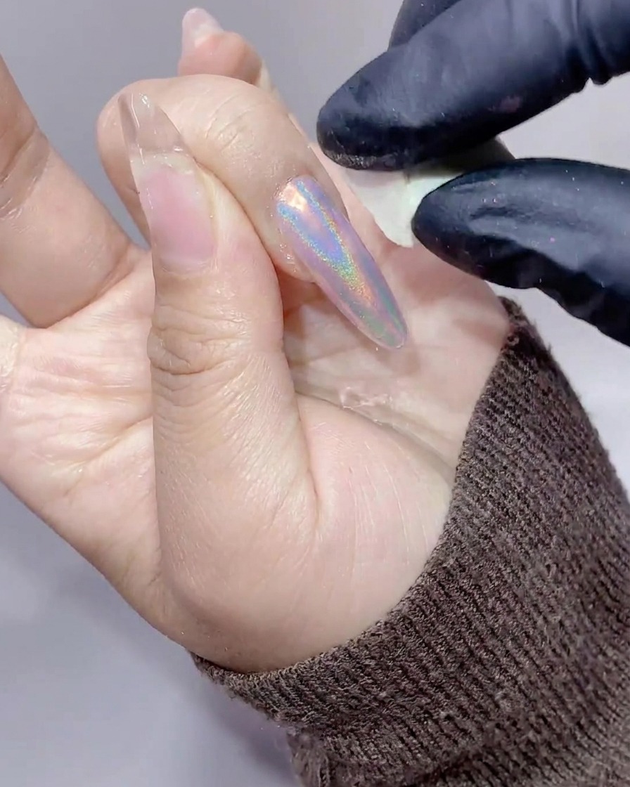 Gros plan dun ongle long débarrassé de lexcès de poudre aurora avec une petite éponge de maquillage blanche.