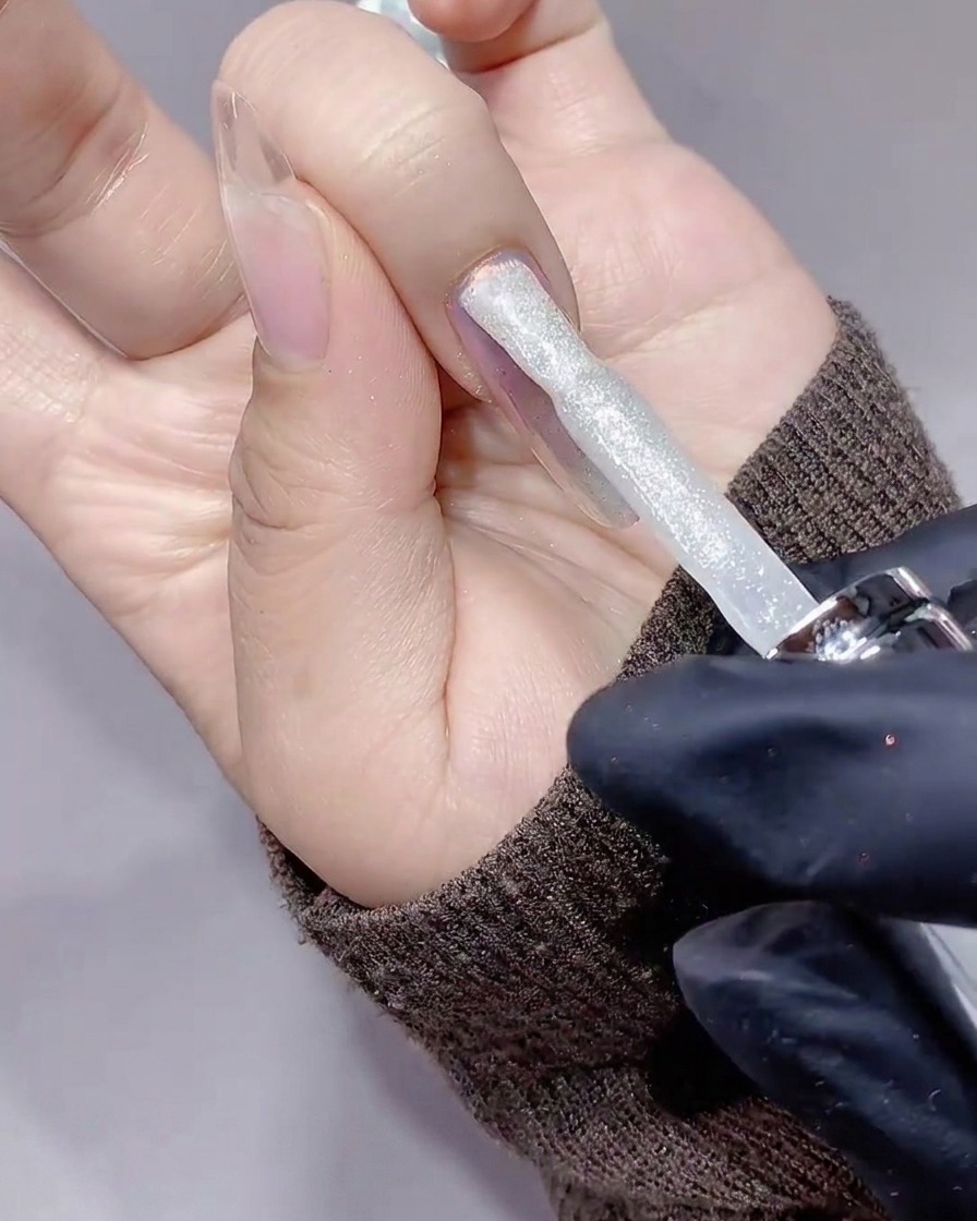 Un pinceau appliquant un gel pailleté diamant argenté sur un ongle.