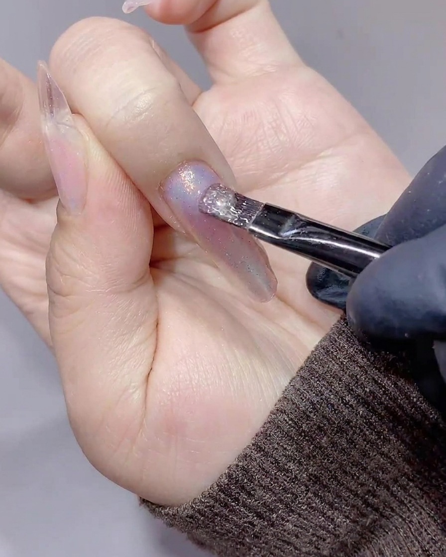 Un pinceau appliquant un gel magnétique cat-eye transparent et scintillant.
