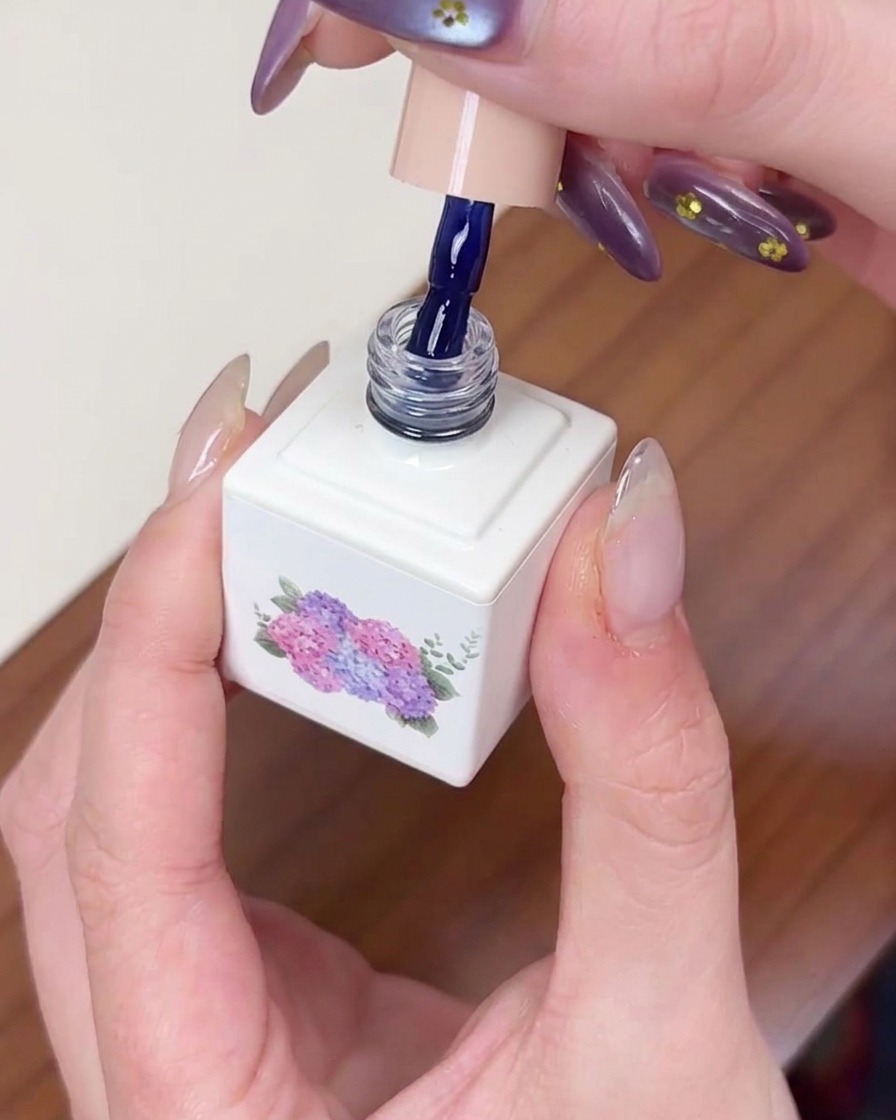 Un pinceau appliquant du vernis gel bleu foncé sur un ongle préparé, assurant une couverture uniforme.
