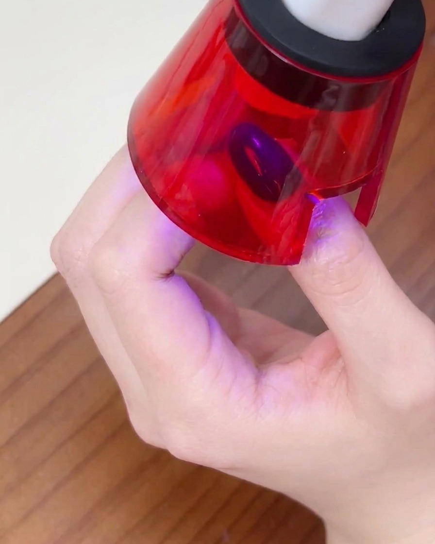Une main positionnée à lintérieur dune petite lampe UV pour ongles, avec le doigt centré pour catalyser le vernis.