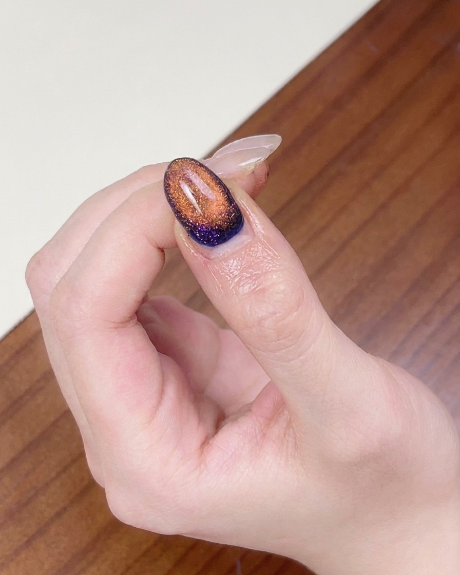 Un doigt placé sous une lampe UV pour ongles afin de catalyser le nail art cat eye magnétique terminé.
