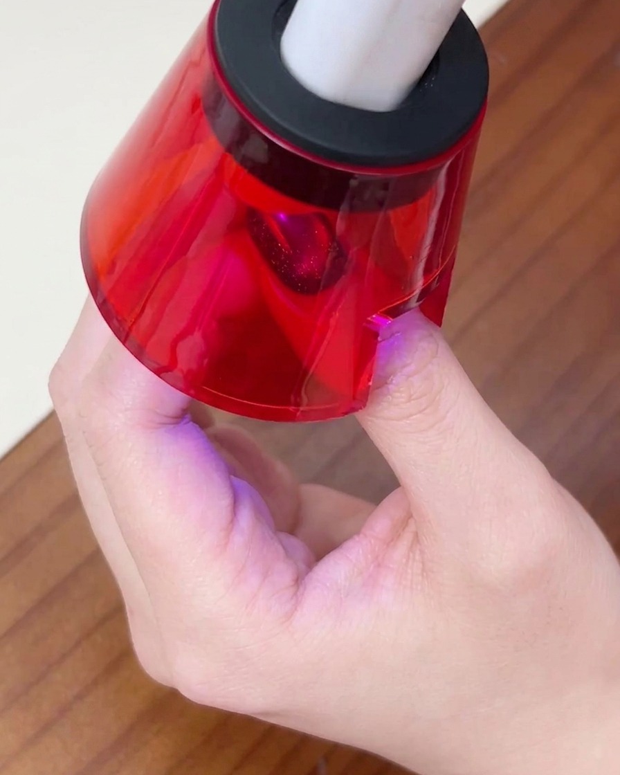 Le doigt dune personne reposant sous une petite lampe à ongles UV/LED rouge pour catalyser la dernière couche de gel.