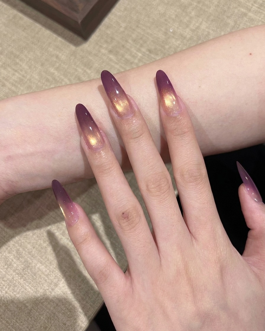 Une main avec des ongles dégradés violet et or placée dans une lampe UV professionnelle pour catalyse.