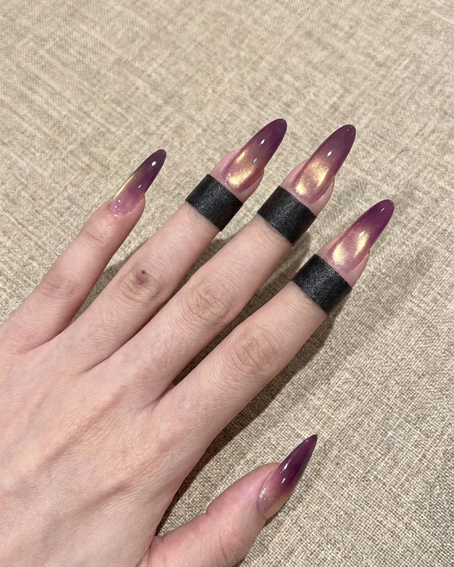 Gros plan dun pinceau appliquant une couche de finition transparente brillante sur un ongle cat-eye dégradé violet et or.