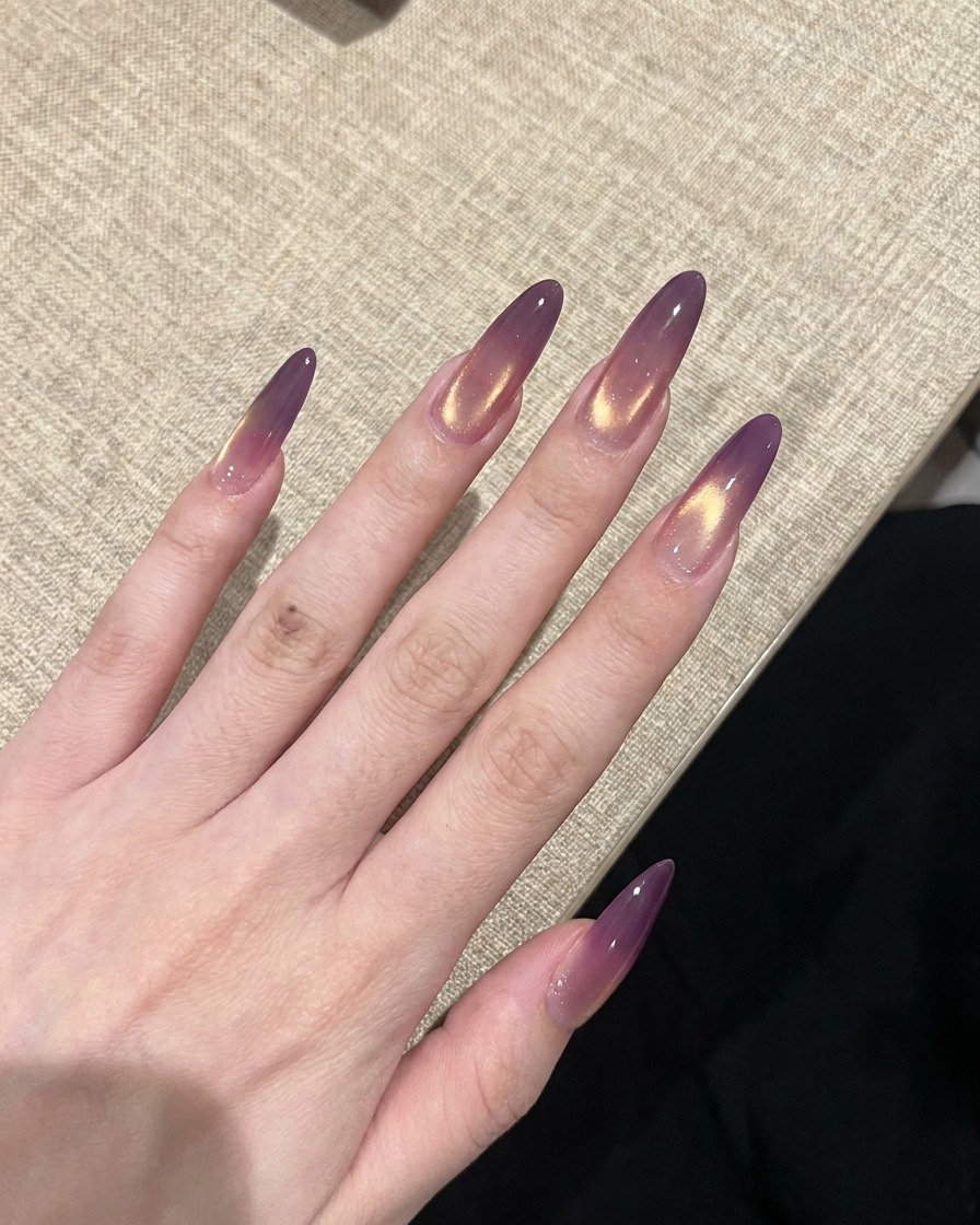 Une main avec des ongles cat-eye dégradés violet et or en finition en cours de catalyse sous une lampe UV.