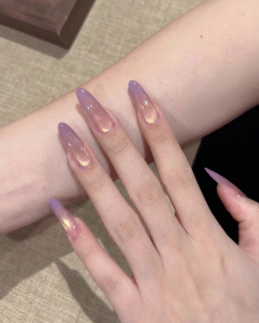 Gros plan sur un pinceau plat déposant une petite goutte de gel violet translucide sur la pointe dune extension dongle stiletto transparente.